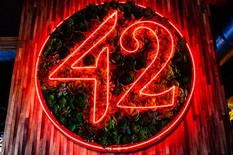 Close-up of the neon 42 sign framed by red-lit succulents on a reclaimed wood wall at Tap 42 Doral