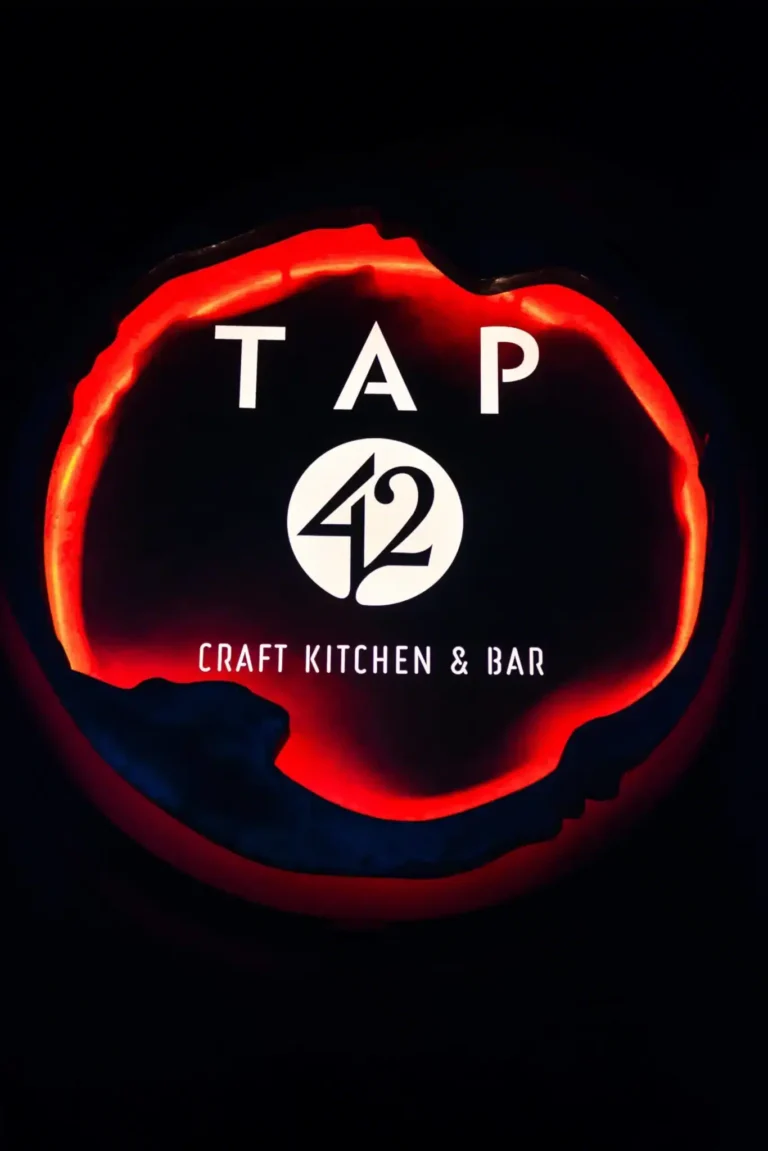 Red-backlit Craft Kitchen & Bar logo sign glowing against a dark wall at Tap 42 Doral