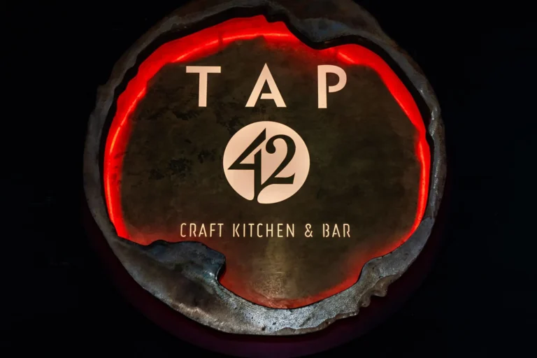 Close-up of the rough-edged metal logo disc ringed in red light at Tap 42 Doral