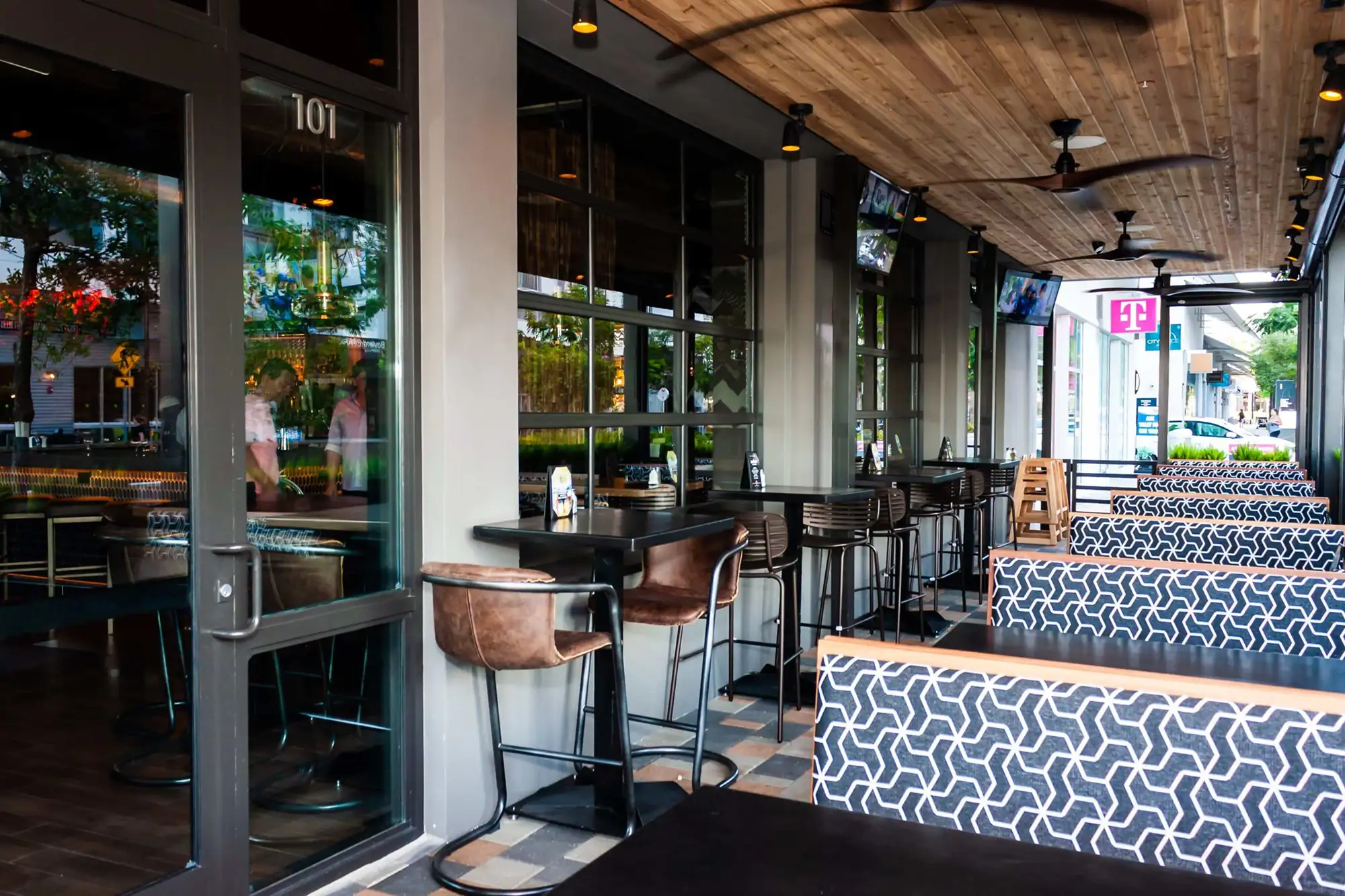 Covered sidewalk patio with high-tops, leather bar chairs, ceiling fans and TVs at Tap 42 Doral