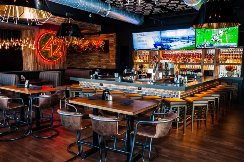 Leather high-top seating leading to the hex-tile bar under three football broadcasts at Tap 42 Doral