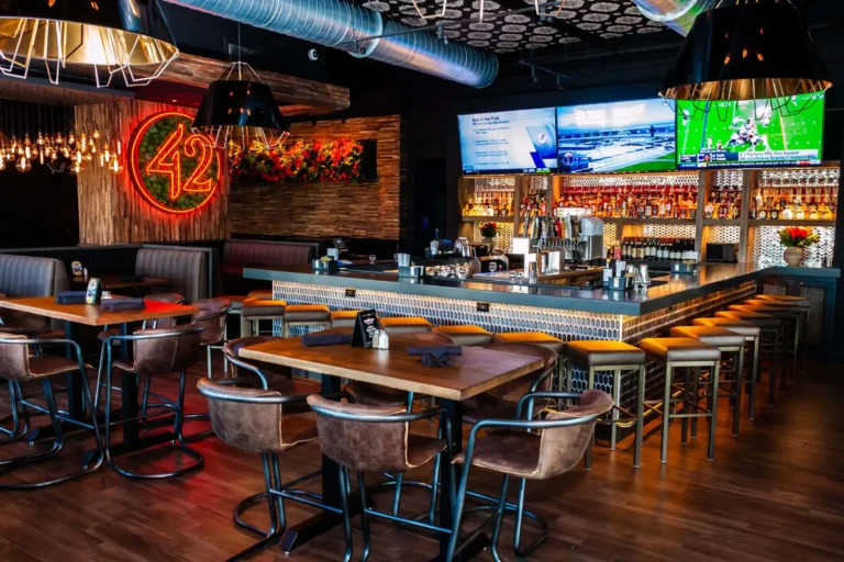 Leather high-top seating leading to the hex-tile bar under three football broadcasts at Tap 42 Doral