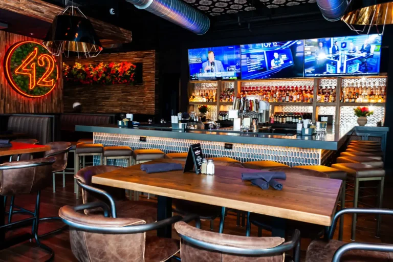 Close view of a set high-top with napkins and menu card facing the bar and TVs at Tap 42 Doral