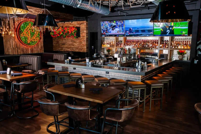 Wide shot of the dining room and bar with black pendant lamps and a wall of TVs at Tap 42 Doral