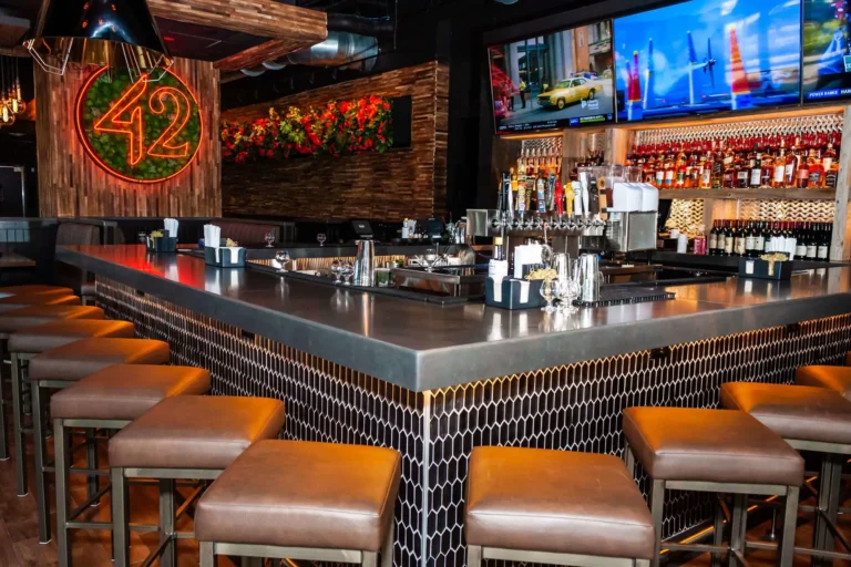 Bar corner close-up showing beer taps, black hex-tile front and brown leather stools at Tap 42 Doral