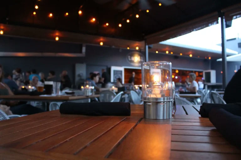 Candle on a wood table with guests under string lights in the covered patio at Tap 42 Fort Lauderdale
