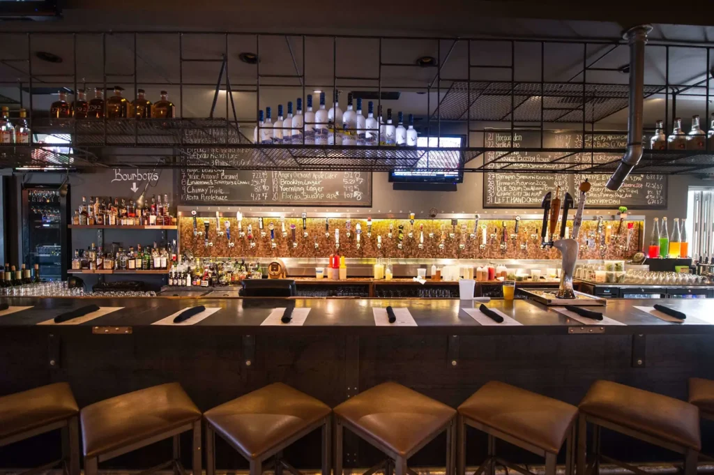 Leather bar stools facing beer taps on a penny wall with bourbon shelves and chalkboards at Tap 42 Fort Lauderdale