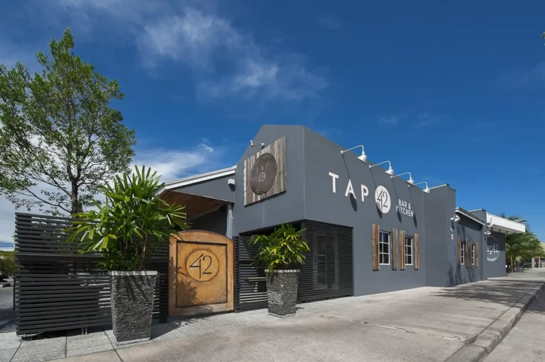 Daytime exterior with a wooden 42 gate, potted plants and slatted fence at Tap 42 Fort Lauderdale