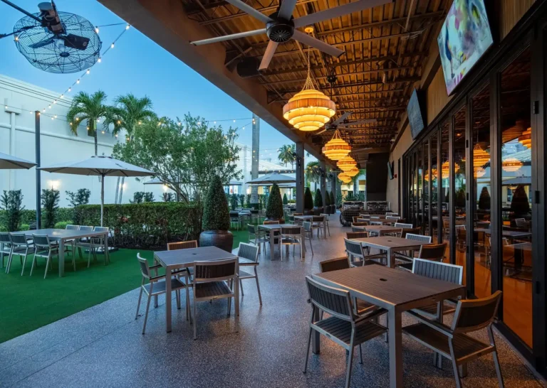 Covered patio at dusk with outdoor tables, ceiling fans and woven pendant lights at Tap 42 Fort Myers