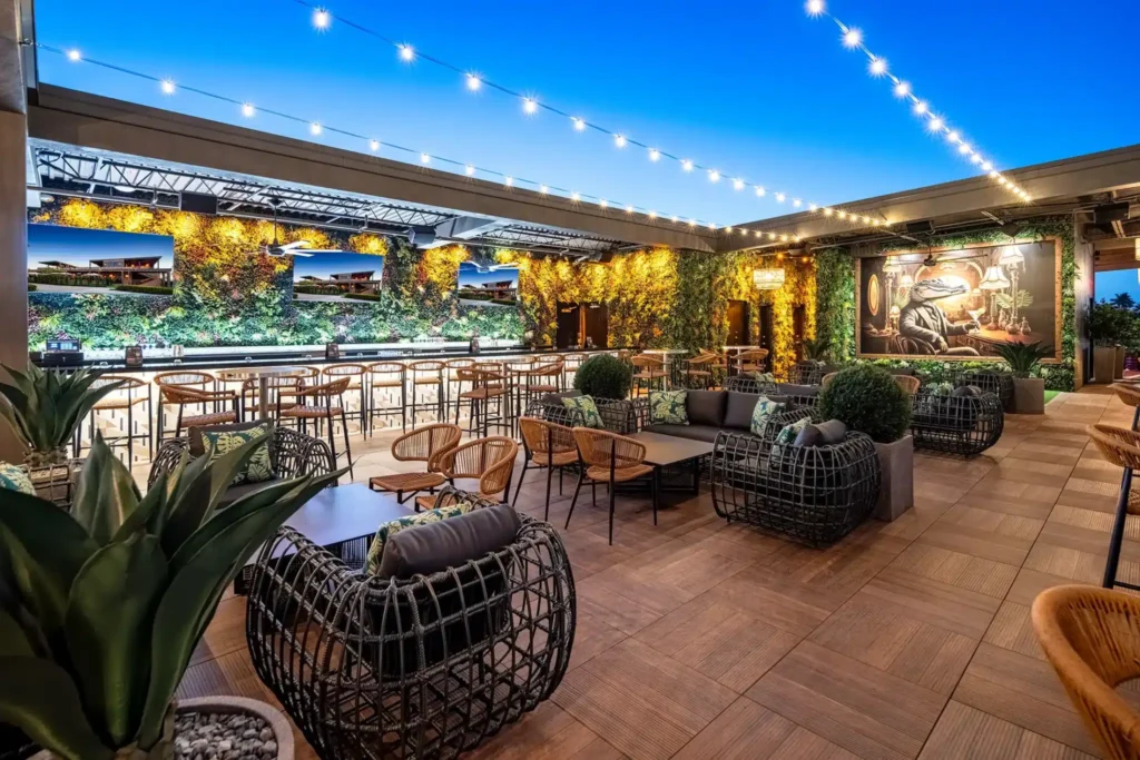 Rooftop lounge at dusk with string lights, TVs on a green wall and an alligator mural at Tap 42 Fort Myers