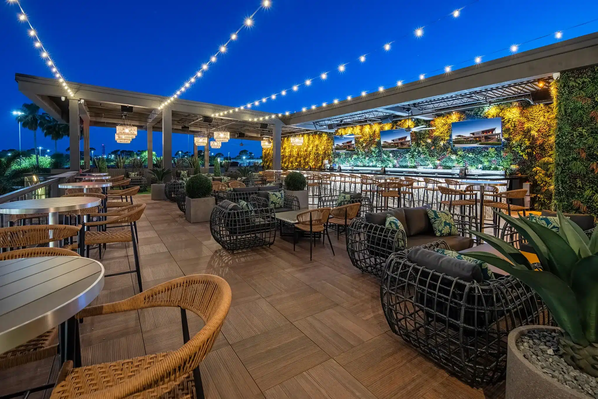 Rooftop bar at night with string lights, wicker lounge chairs and a living green wall at Tap 42 Fort Myers