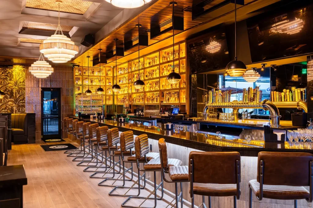 Bar with leather stools, brass beer taps and backlit liquor shelves under tiered pendants at Tap 42 Fort Myers