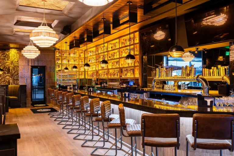Bar with leather stools, brass beer taps and backlit liquor shelves under tiered pendants at Tap 42 Fort Myers