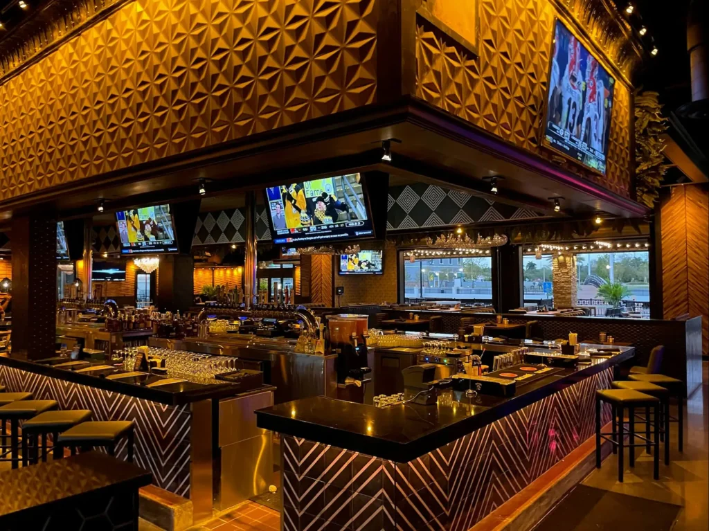 Center bar with chevron front, TVs showing football and gold geometric walls at Tap 42 Kendall