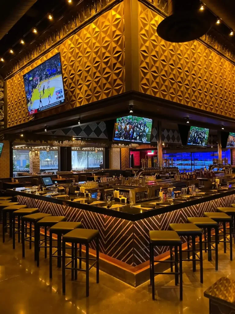 Corner of the bar lined with stools under gold geometric panels and sports TVs at Tap 42 Kendall