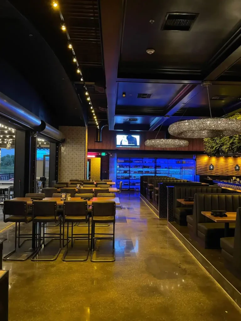 High-top tables by open patio doors with booths and a blue-lit wine wall beyond at Tap 42 Kendall