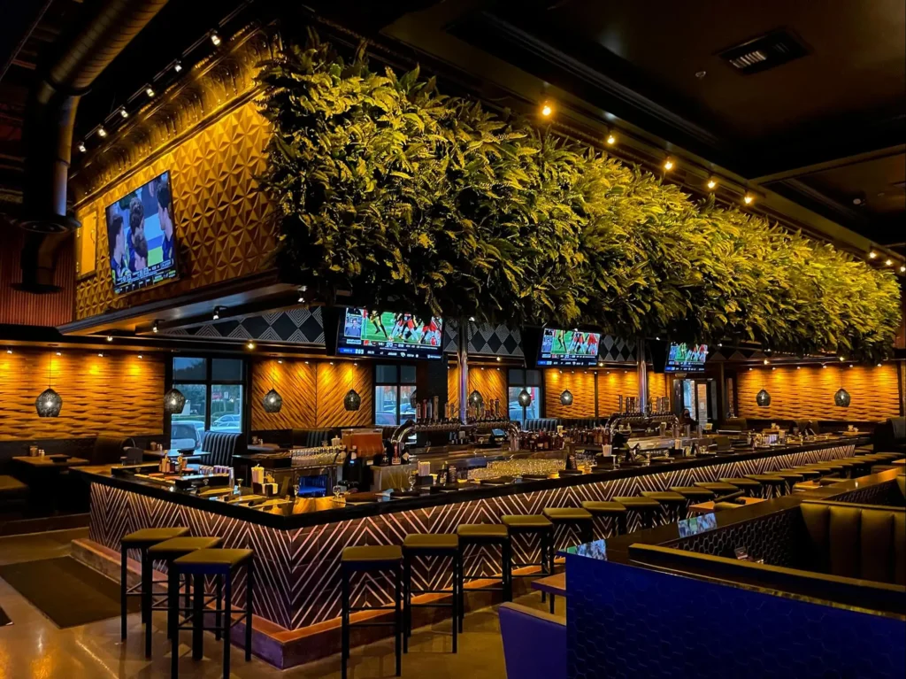 Wide view of the bar with stools beneath a lush living green wall and TVs at Tap 42 Kendall