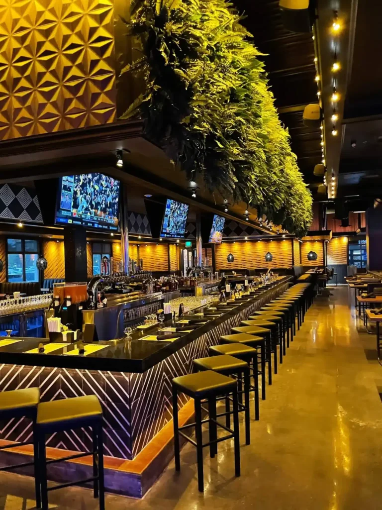 Long row of bar stools under a hanging greenery canopy with high-tops along the side at Tap 42 Kendall