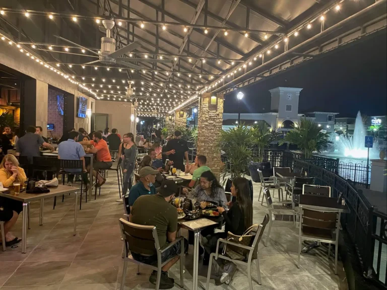 Guests dining under string lights on the covered patio overlooking a lit fountain at Tap 42 Kendall