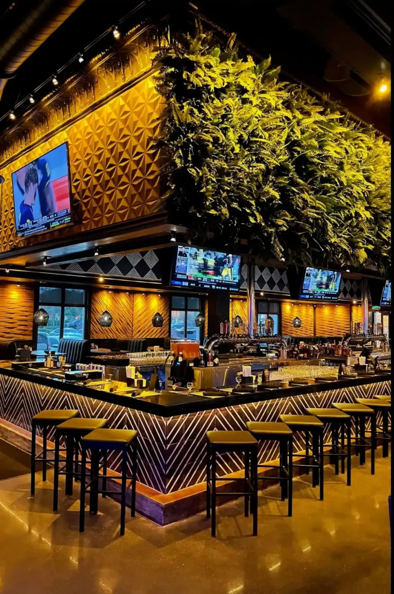 Bar corner lit gold under a green wall canopy with stools and sports TVs at Tap 42 Kendall