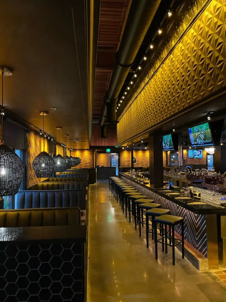Leather booths with woven pendant lamps facing a row of bar stools and gold walls at Tap 42 Kendall