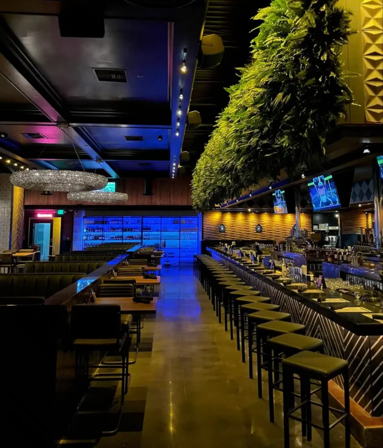 Aisle between bar stools and booths leading to a blue-lit wine wall and chandeliers at Tap 42 Kendall