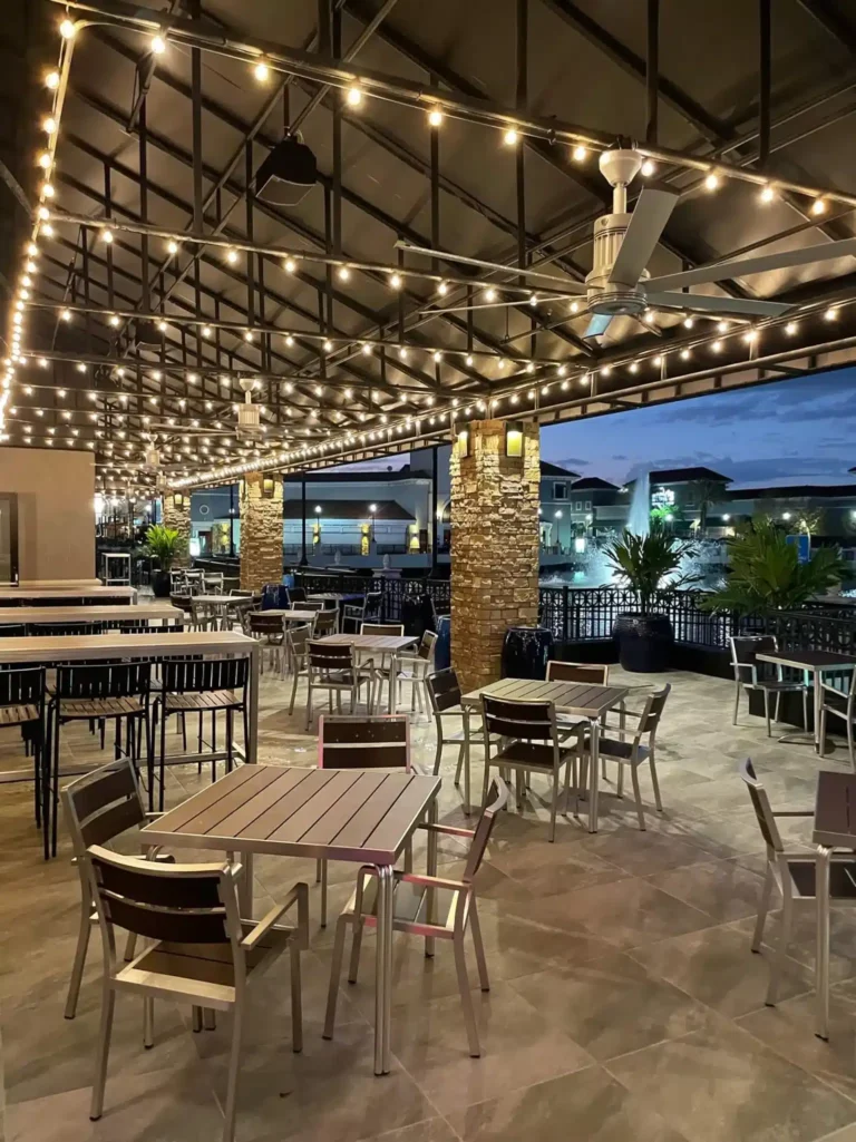 Empty patio tables under string lights and ceiling fans at twilight by the lake at Tap 42 Kendall