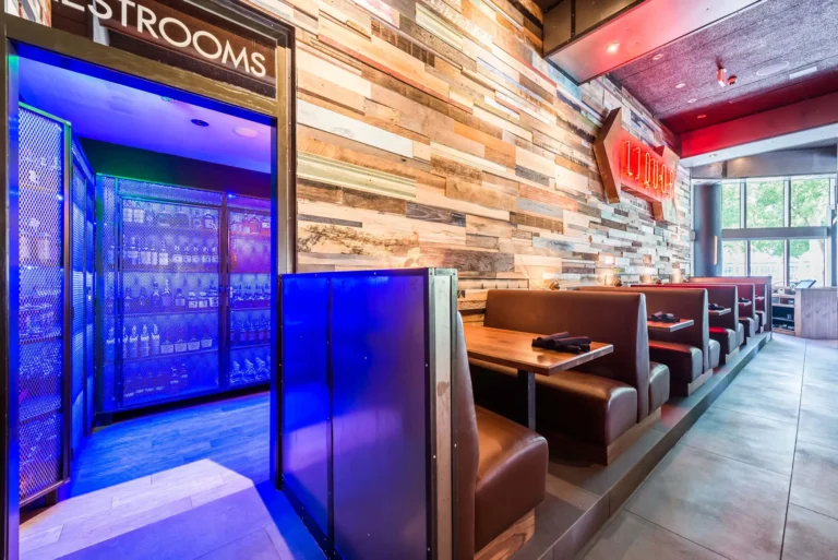 Blue-lit liquor display by the restrooms beside raised leather booths at Tap 42 Midtown Miami