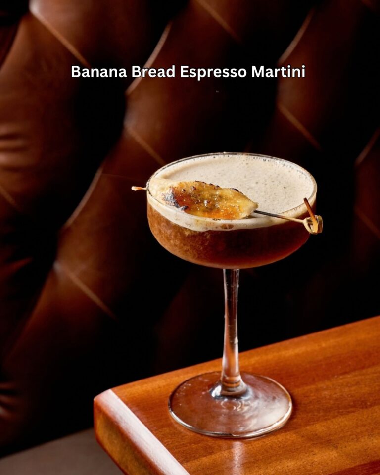 Banana Bread Espresso Martini topped with a caramelized banana slice on a pick, in a coupe glass in front of a tufted leather booth at Tap 42